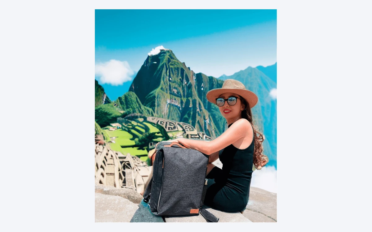Booth.ai example image of a woman in a straw hat and black dress sitting beside a grey backpack, with Machu Picchu ruins and mountains behind her