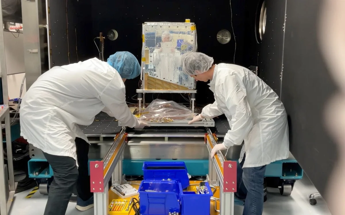 Two technicians in cleanroom gowns positioning the Project Suncatcher prototype satellite inside a thermal vacuum chamber