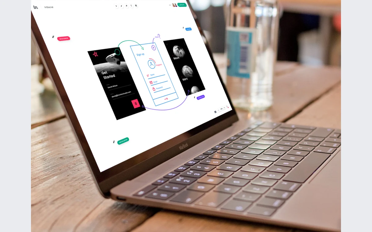 Laptop showing an InVision Freehand canvas with mobile sign-up screen designs, hand-drawn arrows and designer and developer labels