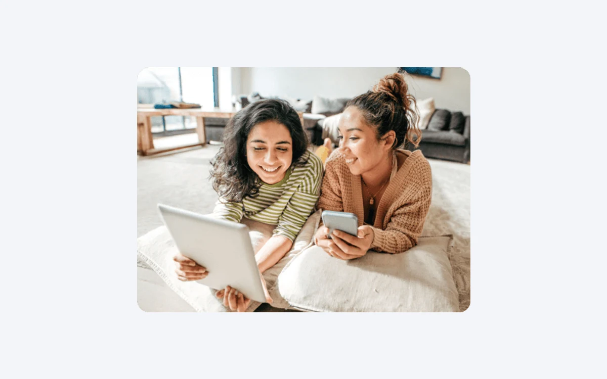 Two women lying down together, one with a tablet and one with a phone, from McAfee's free trial promotion